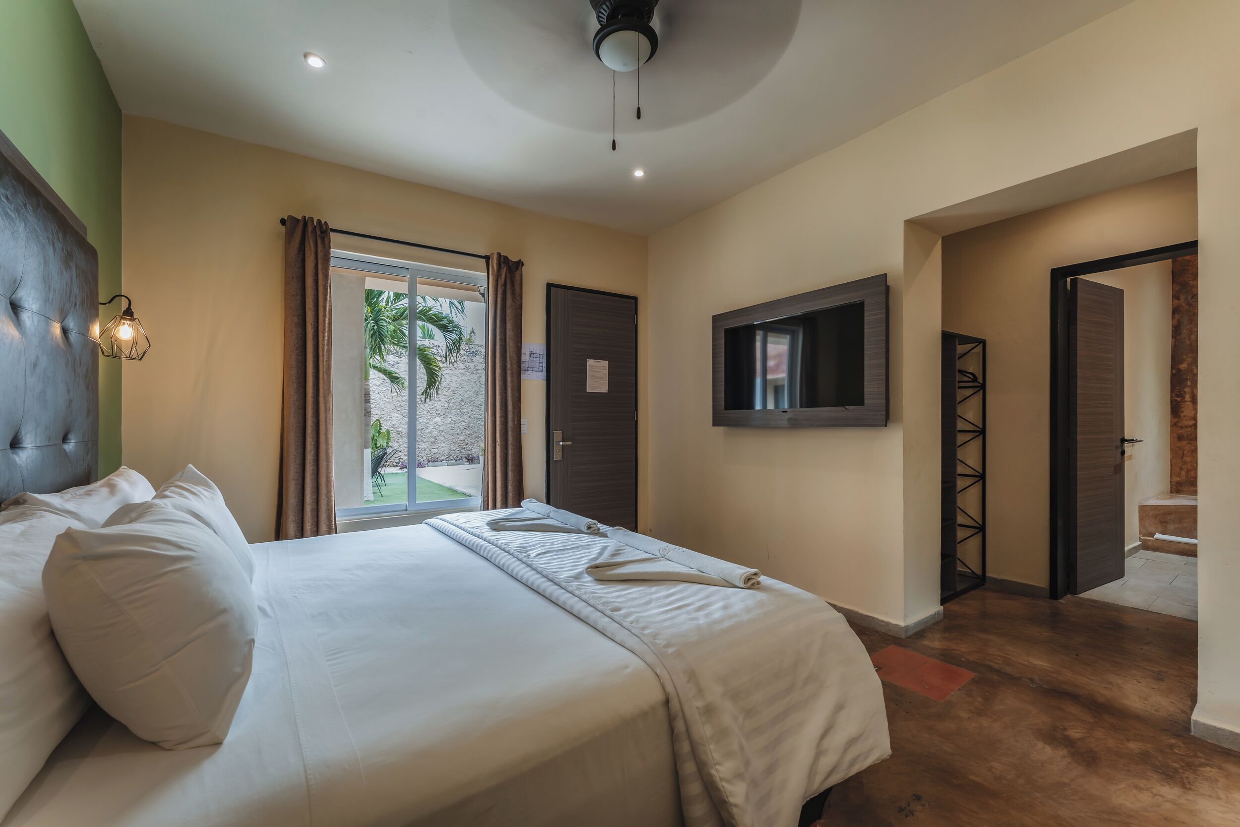 A hotel room with a bed, a television, and a view of the outdoors.