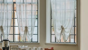 Un comedor con dos ventanas, cafetera, radio y una mesa servida con platos y tazas.