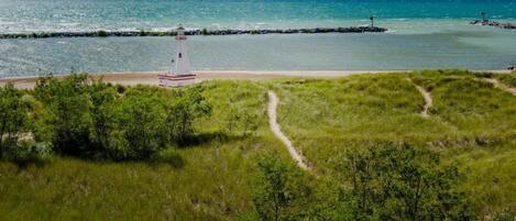 A lighthouse on a grassy hill overlooking a beach with a clear view of the ocean.
