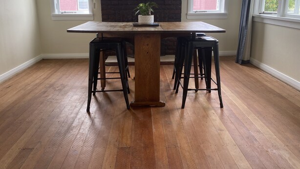 Un coin repas avec une table en bois, quatre tabourets de bar noirs, une plante en pot et une cheminée en briques.