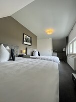 Habitación de hotel con dos camas, un cuadro en la pared, una mesita de noche con lámpara y una ventana con cortinas.
