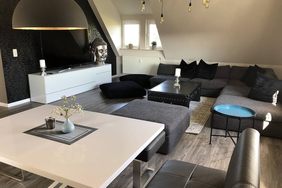 A modern living room with a white sofa, a black coffee table, and a white dining table.