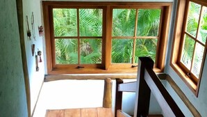 Una escalera de madera conduce a un balcón con ventanas amplias que dan a un paisaje verde exuberante.