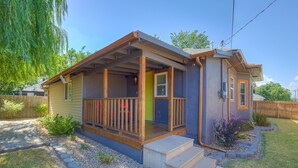 Une maison de plain-pied avec un porche à l’avant, un petit jardin devant la maison avec un chemin, et une clôture en bois.