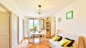 A cozy living room with a sofa, a dining table with chairs, and a kitchen area with a cabinet. - RENTALS-06 NOELIE'S HOUSE - 300M RIVIERE 30mn NICE CANNES ANTIBES (Le Bar-sur-Loup)