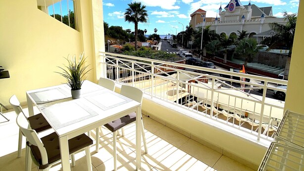 A balcony with a table and chairs, a potted plant, and a view of a castle-like building. - Ocean Golf & Country Club J&K A4 (Oasis del Sur)