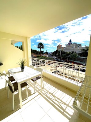 A balcony with a table and chairs, a potted plant, and a view of a castle-like building.