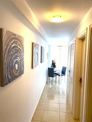 A hallway with a dining area, featuring a table and chairs, and artwork on the walls.