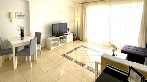 A modern living room with a flat-screen TV, a dining table with chairs, a sofa, and a coffee table. - Ocean Golf & Country Club J&K A4 (Oasis del Sur)