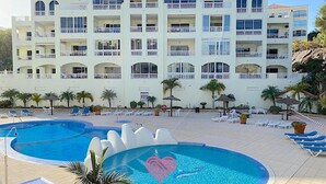 A resort with a large swimming pool, multiple balconies, and a building with a tiled roof. - Ocean Golf & Country Club J&K A4 (Oasis del Sur)