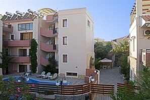 A multi-story hotel with balconies, a swimming pool, and outdoor seating. - Medousa (Platanias)