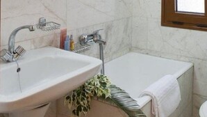 Un baño con un lavamanos de mármol, una bañera, un armario de madera sobre el lavamanos y una ventana.