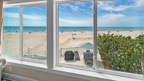A view from a window overlooking a beach with a deck area featuring outdoor furniture.