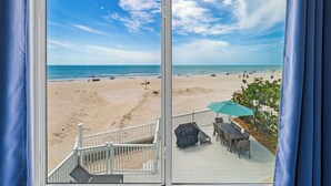 A beach view through a window with a white railing and a covered patio area.