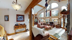 A spacious living room with a fireplace, wooden beams, and large windows offering views of the outdoors. - Views | Hot Tub | Fireplace | Scenic Serenity (Angel Fire)
