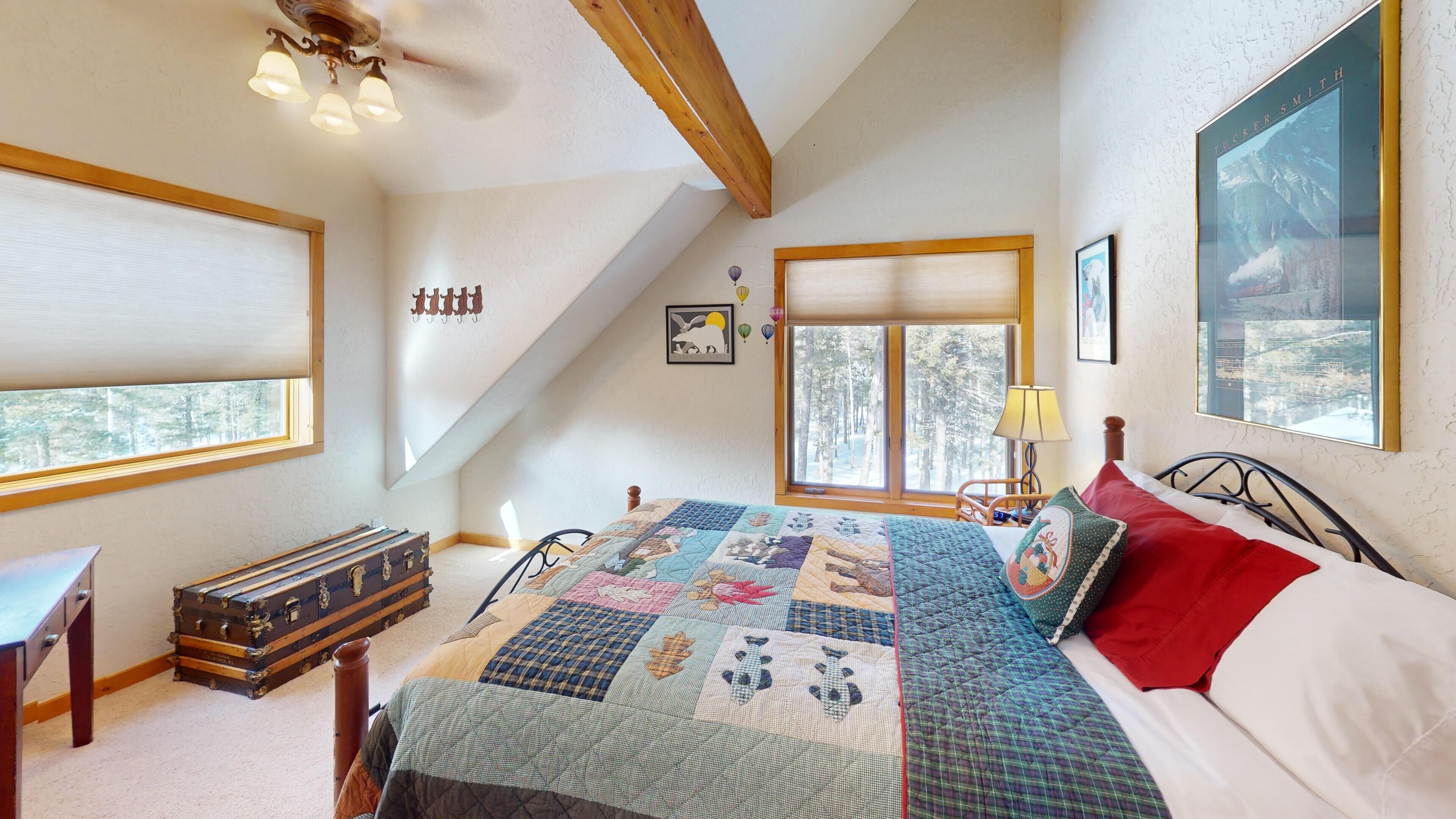 A bedroom with a large bed, a wooden headboard, a window with a view of trees, a lamp, and a suitcase.