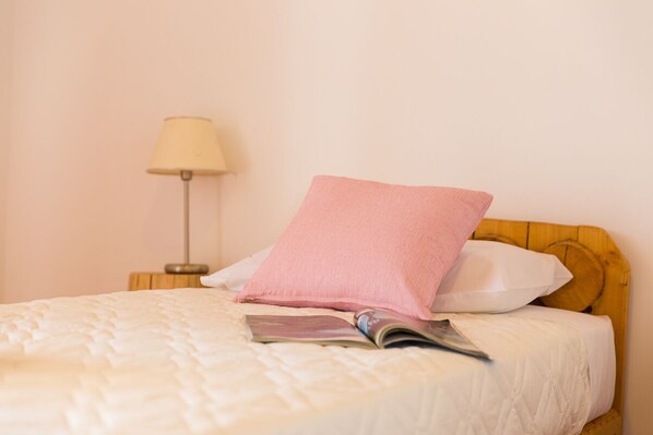 A neatly made bed with a white quilt, a pink pillow, and a white pillow on a wooden headboard.