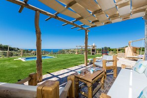 En træpergola med pool og udendørs siddeområde.