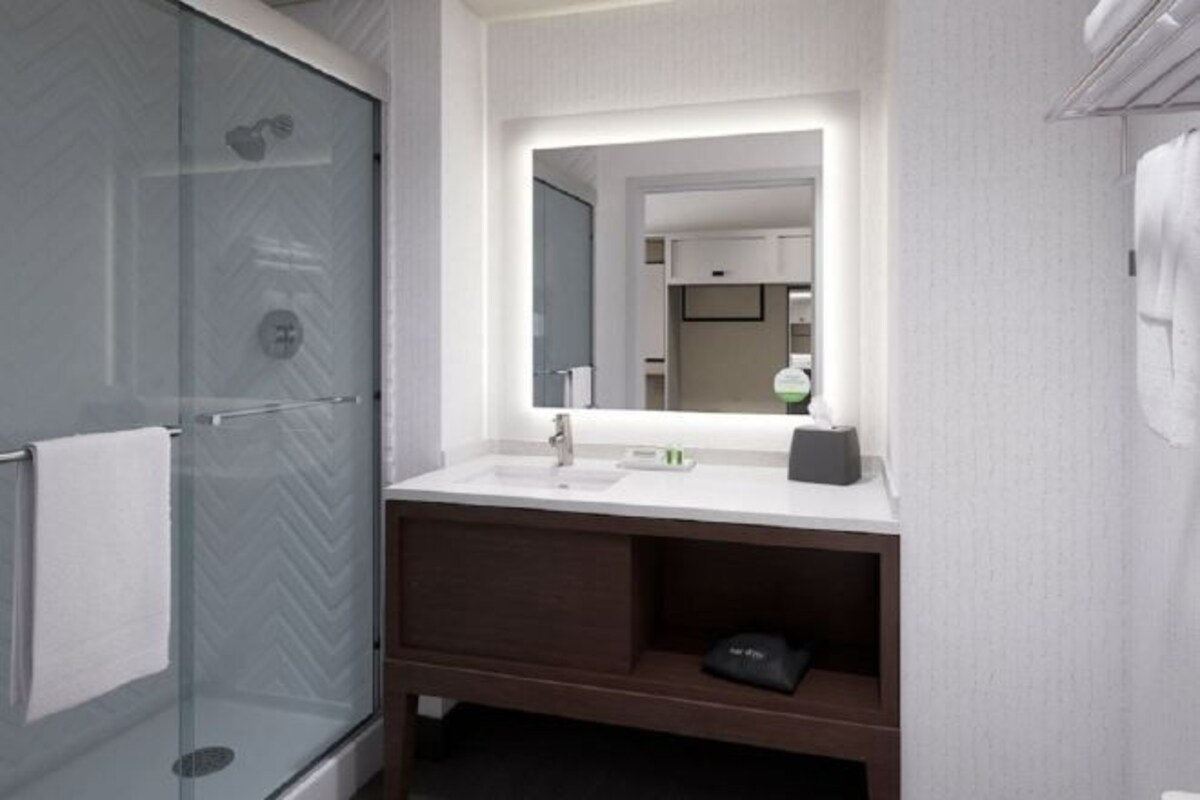 Een moderne badkamer met een glazen douchecabine, een witte wastafel met spiegel erboven en een donker houten opbergmeubel.