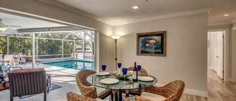 Un coin repas avec une table en verre, des chaises en osier et une vue sur la piscine.