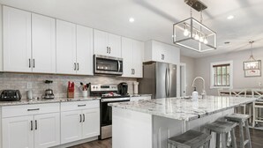 A modern kitchen with white cabinetry, a large island with stools, stainless steel appliances, and a pendant light.