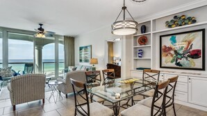 Een ruime woonkamer met een grote glazen tafel en stoelen, een bank en uitzicht op de oceaan.