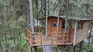 Een houten boomhut met een houten terras en een touw-brug.