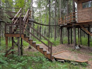 A wooden cabin with a staircase leading to a platform, surrounded by a forest. - Time for adventure. Sleep in a treehouse. 5 minutes from the airport & downtown! (Fairbanks)