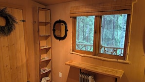 Een houten interieur met een raam dat uitkijkt op een bos, een radiator, een plank en een ladder.