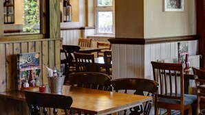 Een restaurant interieur met houten tafels en stoelen, een menukaartstandaard en een raam met uitzicht op groen.