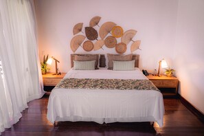 Un lit bien fait, recouvert d’une courtepointe blanche et agrémenté de deux oreillers, un mur orné d’un motif décoratif en forme de feuilles, et deux tables de chevet avec des lampes et une plante.