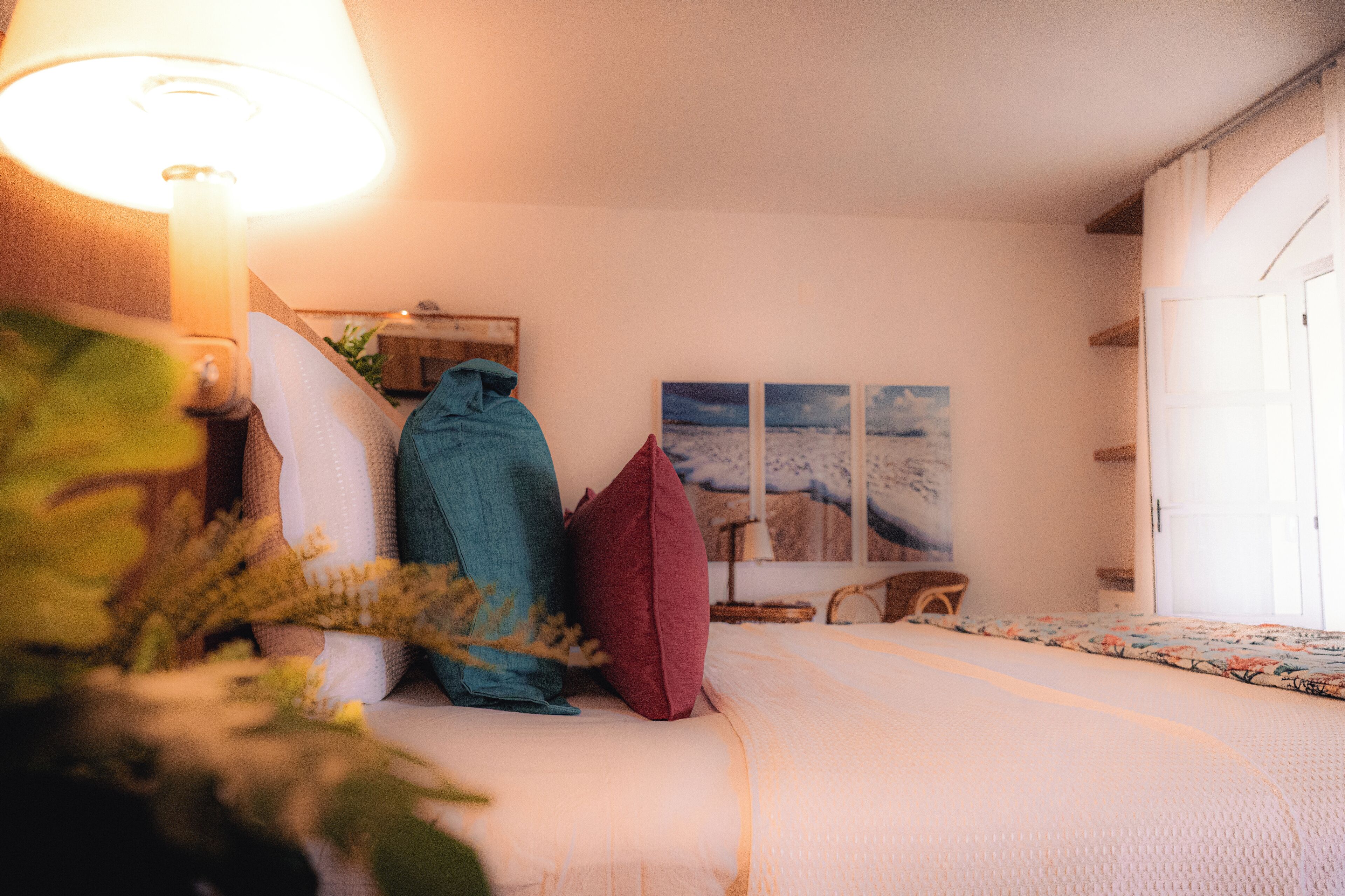 Una camera da letto con un letto, cuscini, una lampada e un quadro appeso al muro.