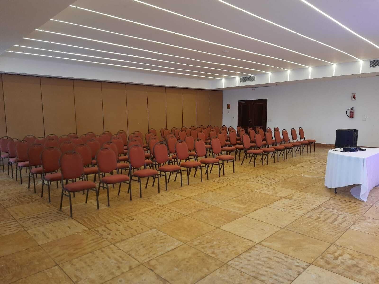A conference room with rows of red chairs, a white table with a projector, and a tiled floor.