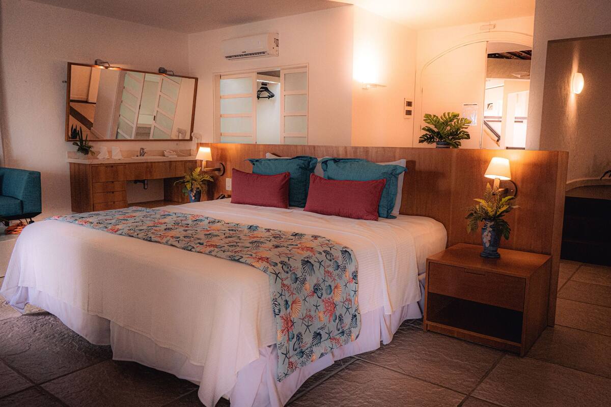 A neatly arranged bedroom with a large bed, bedside tables with lamps, a wooden headboard, and a mirror above the bed.