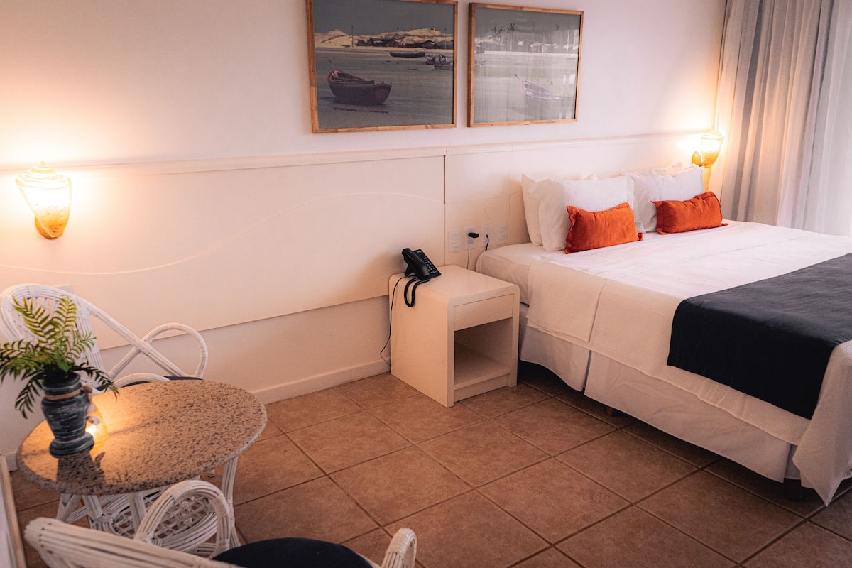 A hotel room with a bed, bedside table, chair, and a small table with a plant.