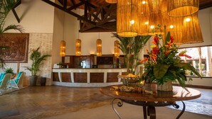 A lobby with a reception desk, hanging wicker chandeliers, and tropical plants. - Sun City Rota das Emoções (Camocim)