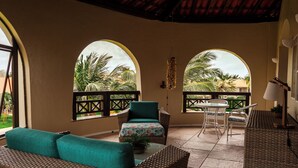 A sunlit patio with wicker furniture, a table, and a view of palm trees. - Sun City Rota das Emoções (Camocim)