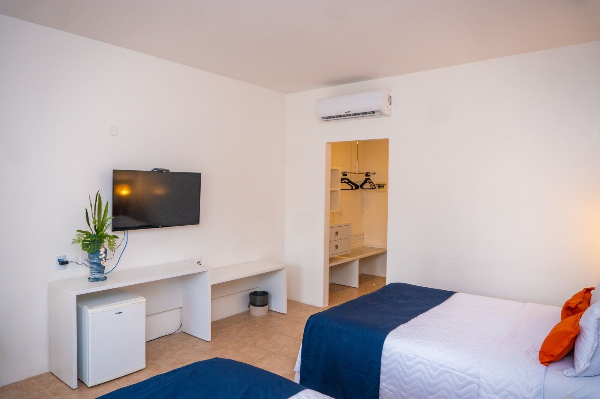 Una habitación de hotel con cama, escritorio con refrigerador pequeño, televisor y vestidor.