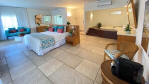 A hotel room with a bed, a sofa, a chair, a desk, a mirror, a bathroom with a bathtub, and a shower. - Sun City Rota das Emoções (Camocim)
