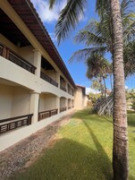 Un edificio con techo de tejas, varios balcones con barandillas de madera y un césped cuidado con palmeras.