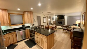 A modern kitchen with wooden cabinets, a central island, and a dining area with a fireplace. - August Special, Great Rates! Locking bike storage! (Gunnison)
