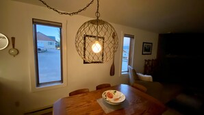 A dining area with a wooden table, a hanging light fixture, and a window with a view of the outside. - August Special, Great Rates! Locking bike storage! (Gunnison)