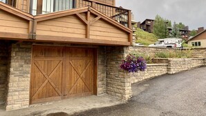A two-story building with a wooden facade, a garage with a large wooden door, and a stone wall with a flower planter. - August Special, Great Rates! Locking bike storage! (Gunnison)