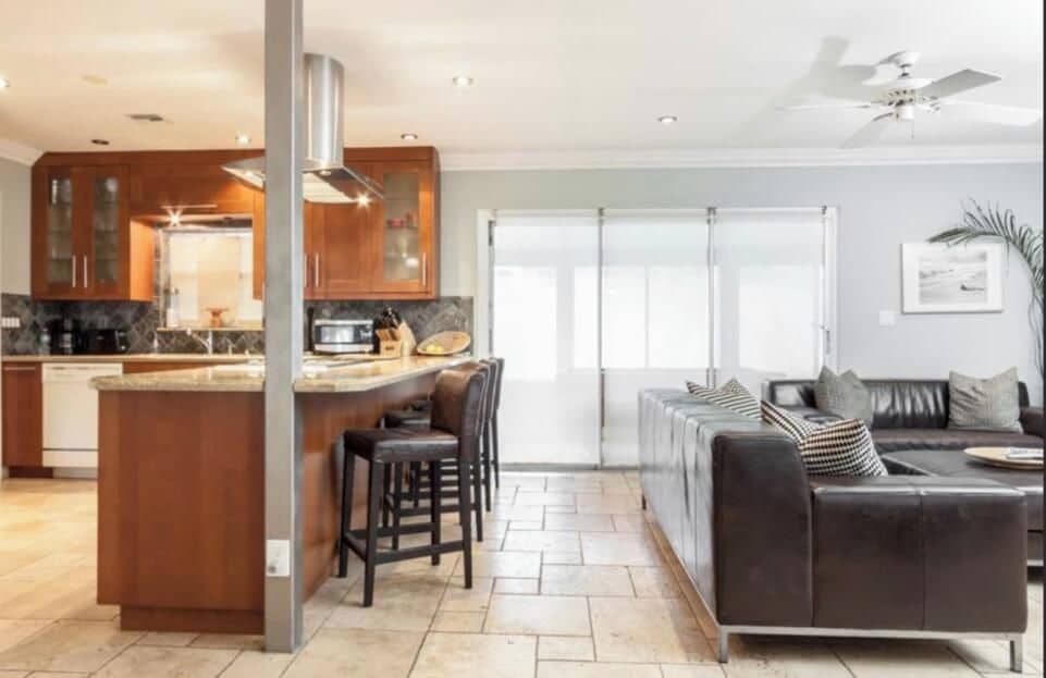 Une cuisine moderne avec un îlot central, des canapés en cuir foncé et une grande porte-fenêtre coulissante donnant sur un balcon.