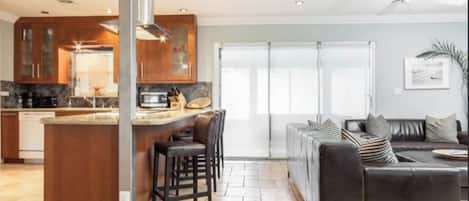 Une cuisine moderne avec un îlot central, des canapés en cuir foncé et une grande porte-fenêtre coulissante donnant sur un balcon.