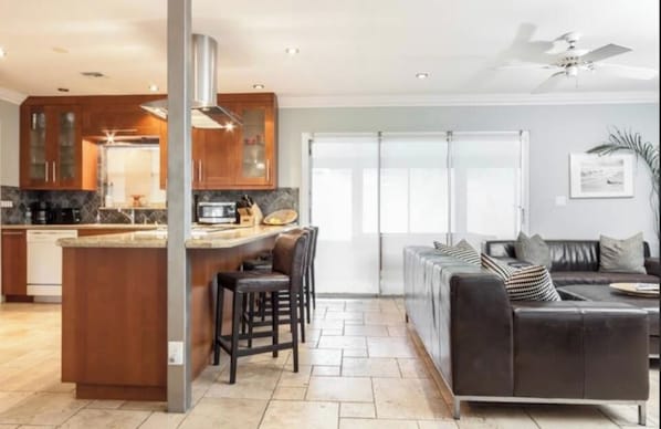 A modern kitchen with a central island, dark leather sofas, and a large sliding glass door leading to a balcony. - Charming Pompano Beach escape, nr ocean and hotspots, Walk to Beach, Hot Tub. (Pompano Beach)
