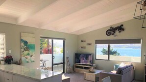 Amplia sala de estar con puerta corredera de vidrio que da a un balcón, un televisor de pantalla plana, un sofá y una mesa de comedor.