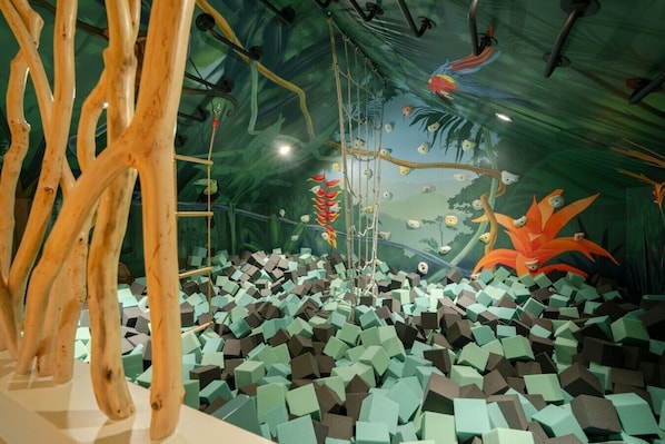 An indoor space with a rope bridge, hanging decorations, and a colorful mural on the wall.