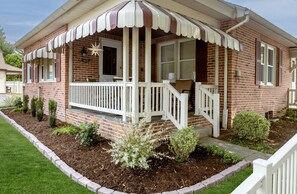 Une maison en briques avec un porche blanc, une boîte aux lettres et un jardin bien entretenu.