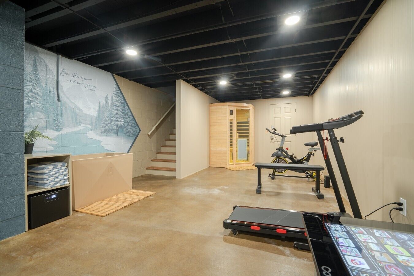 A home gym with exercise equipment, a staircase, and a wall mural.